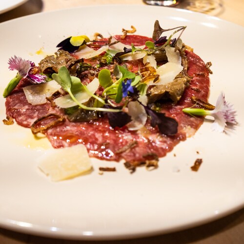 Un carpaccio de bœuf à la truffe recouvert de verdure et de fleurs dans une assiette.