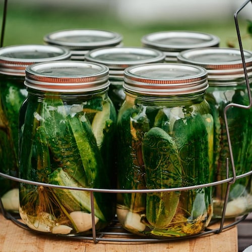 Des bocaux remplis de cornichons à l'aneth dans un panier en fer.