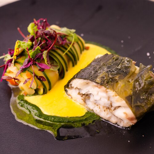 De la morue charbonnière enroulée dans des algues avec un rouleau de ratatouille et de la purée d'épinards dans une assiette.