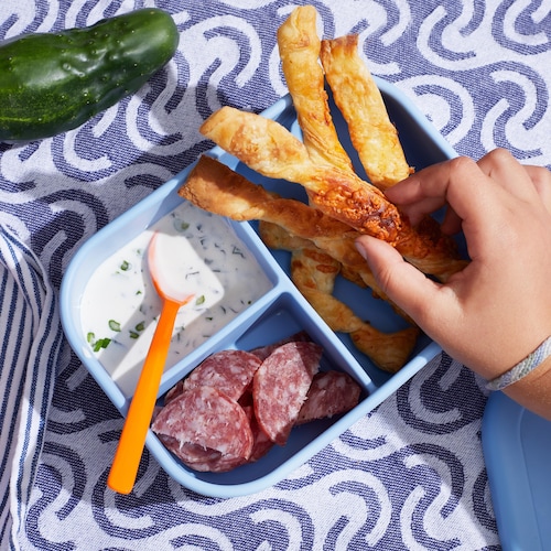 Des pailles au fromage dans un plat. Elles sont servies avec de la trempette et des morceaux de saucisson séché.