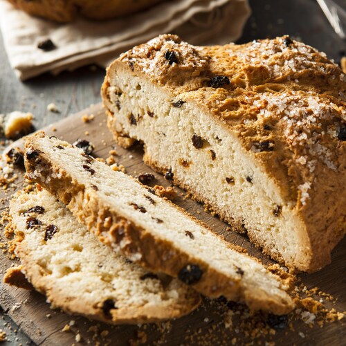 Une miche de pain au soda, parsemée de raisins secs et de gros sel, sur une planche à découper.
