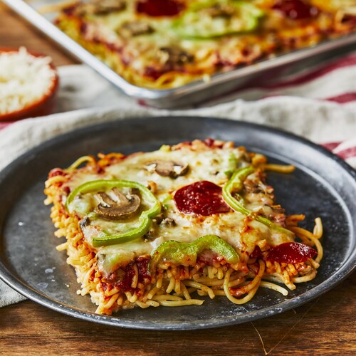Une assiette de pizza-ghetti près d’une plaque de pizza-ghetti, sur une table. 