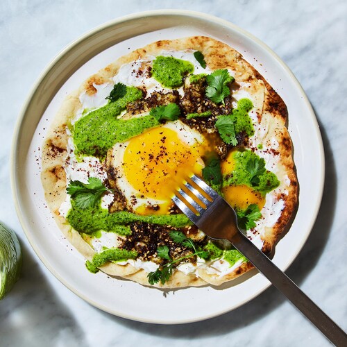 Un pain naan recouvert de fromage à la crème garni d'un œuf frit et de sauce zhoug.