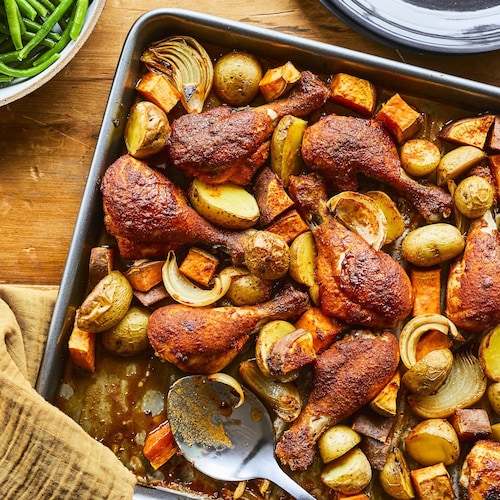 Sur une table en bois, est déposé une plaque à cuisson remplie de pilons de poulet BBQ. 