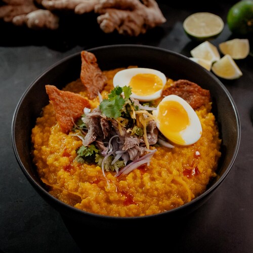 Un bol de porridge de riz au canard confit et au gingembre, garni d'oeufs.