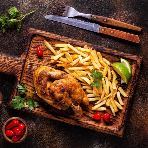 Du poulet piri-piri en demi-crapaudine servi sur une planche, avec des frites et des quartiers de lime.