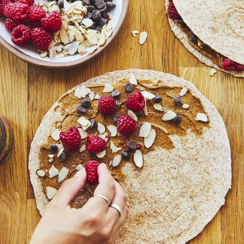 Une main en train de garnir une quesadilla déjeuner de framboises et de tartinade au chocolat. 
