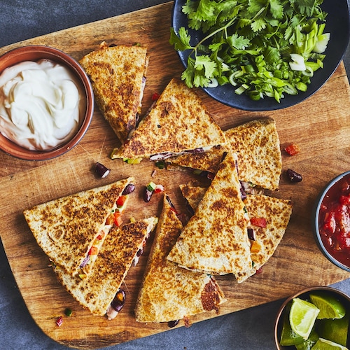 Portions de quesadillas sur une planche en bois avec un bol de salsa et de crème sure.