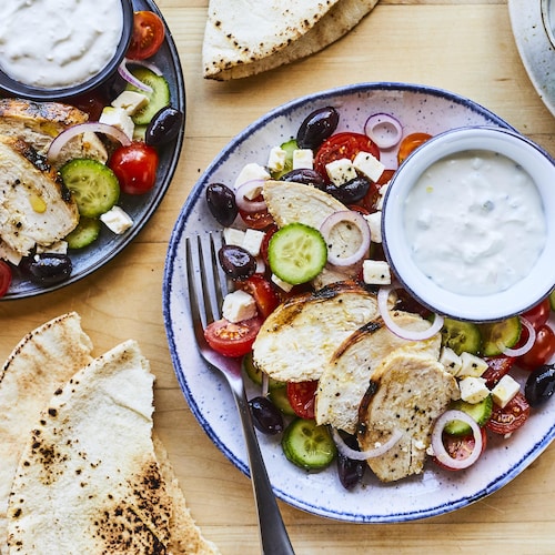 Plusieurs assiettes de salades de poulet grillé à la grecque sur une table avec des pains pitas.