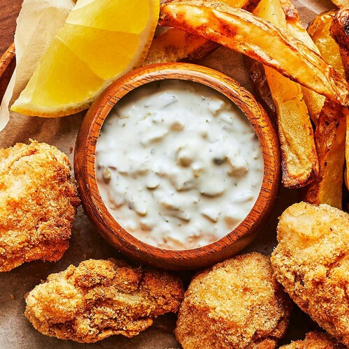 Un bol de sauce tartare accompagne des frites et des bouchées de fish and chips dans une assiette.  