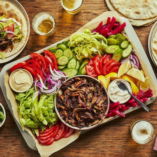 Une planche de légumes variés avec des pains pitas et des champignons shawarma, trois verres de bière et des assiettes de pains pitas garnis.