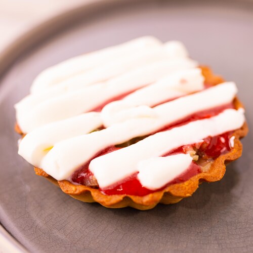 Une tartelette à la fraise, au fenouil et au praliné de noisettes dans une assiette avec de la chantilly sur le dessus.