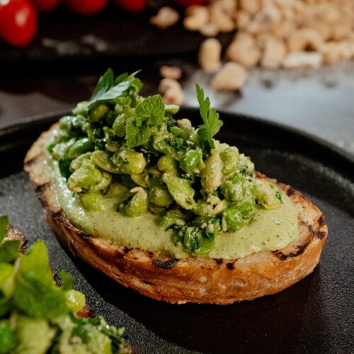 Une tartine recouverte de petits pois et d'herbes fraîches.
