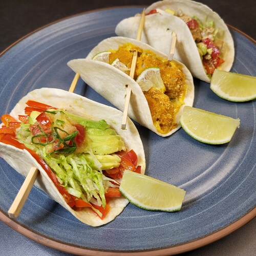 Un taco végétarien, un taco au poisson et un taco au poulet disposés dans une assiette.