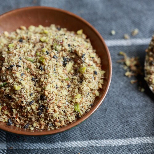 Du dukkah, un mélange d'épices et de noix concassées, dans un bol sur une table.