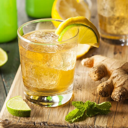 Un verre de soda au gingembre décoré d'une tranche de lime et d'une tranche de citron repose sur une planche en bois. 