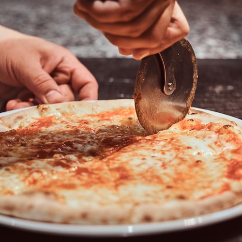 Une personne coupe une pizza margarita avec une roulette à pizza.