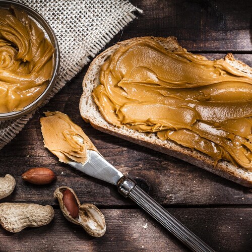 Du pain avec du beurre d'arachide sur une table en bois, avec des cacahuètes et des arachides, et un couteau.