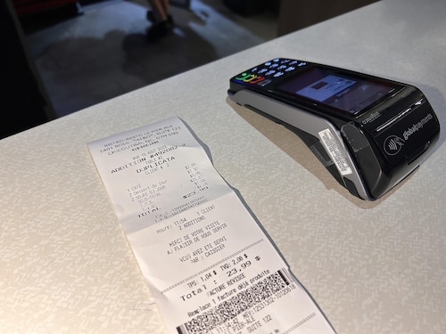 Une facture de restaurant sur une table à côté d'un terminal de paiement électronique.