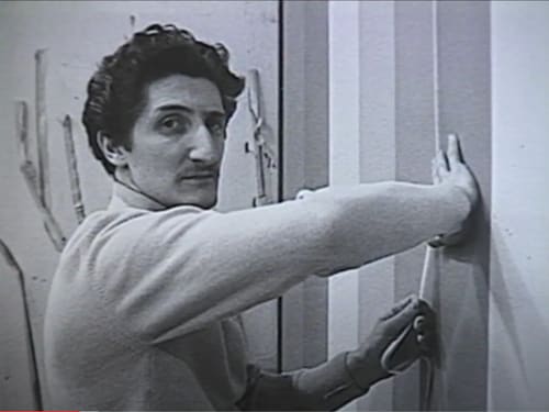 Guido Molinari colle du ruban adhésif sur une toile en regardant la caméra. 