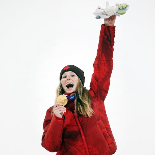 Une femme sourit à pleines dents et tient sa médaille d'or dans sa main droite.