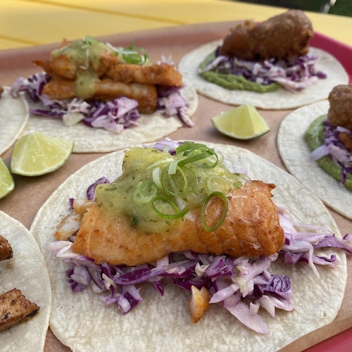 Des tacos de poisson posés sur des tortillas de maïs blanc avec des quartiers de lime et de la salade de choux rouge. 