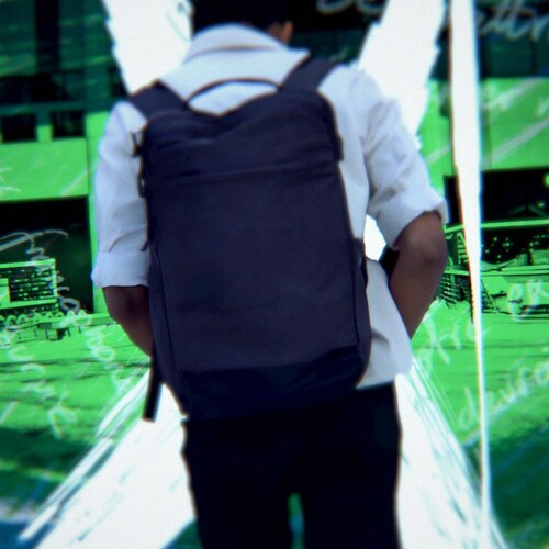 Un jeune homme de dos avec un sac à dos devant l'entrée d'une école.