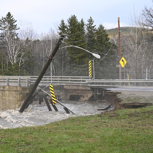 Un lampadaire est penché au-dessus d'une rivière tout à côté d'un pont que les inondations ont lourdement endommagé.