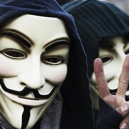 2 Hacktivists Anonymous dont l'un qui fait un signe paix