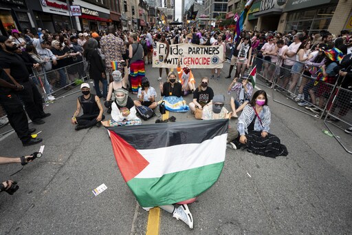 Assis sur la chausse, des manifestants propalestiniens tiennent des drapeaux.