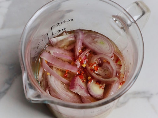 Des morceaux d'échalotes crus flottent dans un liquide à l'intérieur d'une tasse à mesurer.