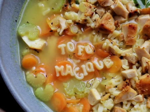 Vue en plongée sur une bol de soupe de tofu avec des nouilles alphabet qui forment les mots « Tofu Magique » sur la surface de la soupe.
