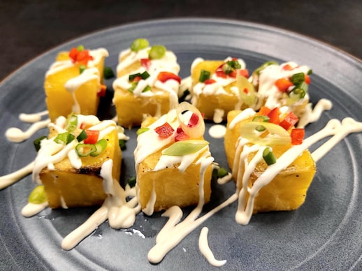 Des cubes de pomme de terre rôtis arrosé d'une sauce crémeuse et garnis de légumes, servis dans une assiette.