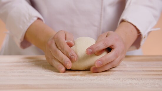 Une personne pétrit une boule de pâte à pain sur un ilot bien enfariné. 