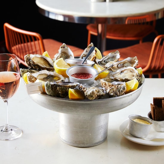 Un plateau d'huîtres ouvertes déposé sur une table, à côté d'un verre de vin rosé et d'une petite assiette de pain. 