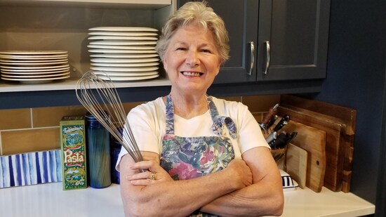 Une femme avec un fouet à la main devant son comptoir de cuisine.