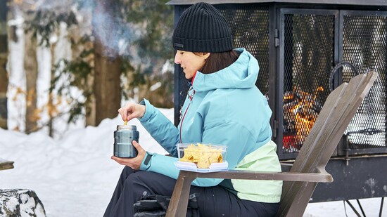 Geneviève O'Gleman est assise sur une chaise dehors dans un contexte de sport d'hiver et mange des nachos.
