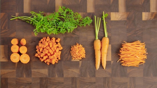 Sur une planche de travail, deux carottes non coupées sont entourées des morceaux de carottes coupés différemment. 