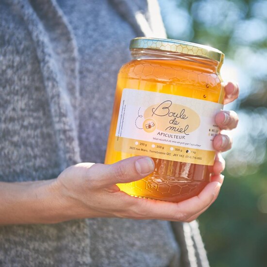 Une personne tient un pot de 1 kg de miel entre ses mains. 