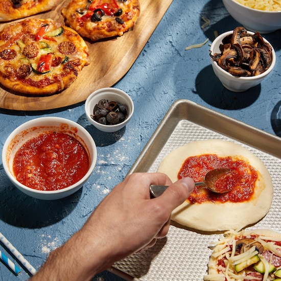 Quelques pizzas garnies sur une planche de bois et des bols de condiments autour. 