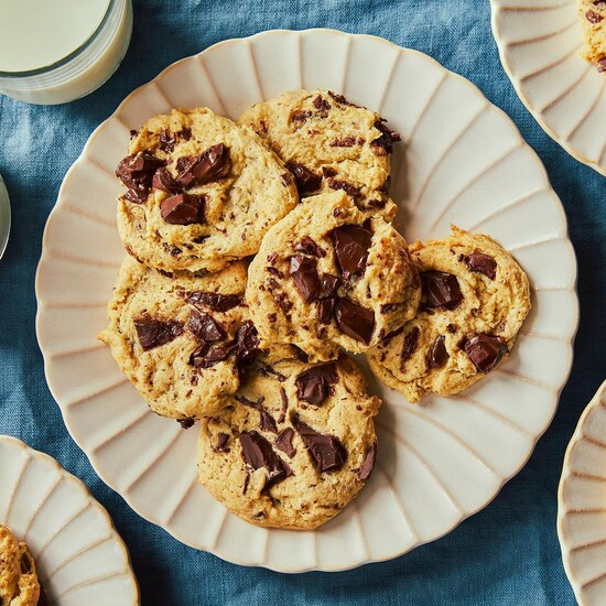 Plusieurs biscuits sont dans une assiette blanche sur une nappe bleue et accompagnés de deux verres de lait.