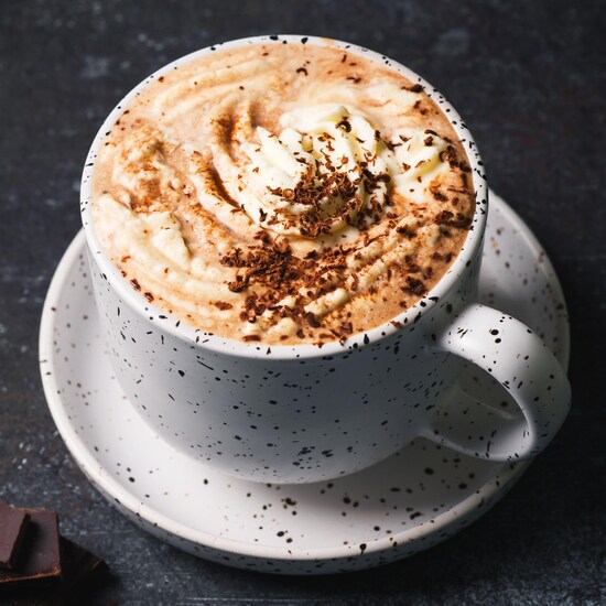 Une tasse dans une soucoupe avec de la crème fouettée et du chocolat râpé. 