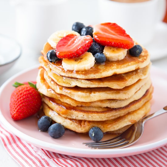 Des pancakes dans une assiette avec des bleuets, des fraises et des bananes.