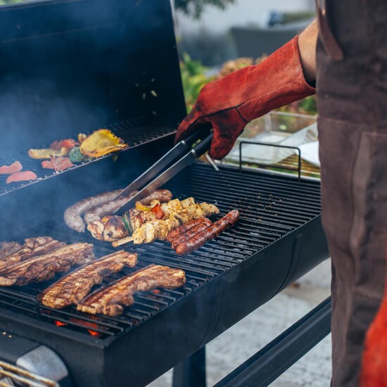 Un homme fait cuire des saucisses, de la viande et des brochettes sur le barbecue.