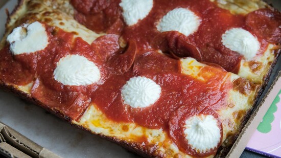 Une pizza avec de la sauce tomate, du fromage gratiné, des rondelles de pepperoni et des petits ronds de crème sure. 