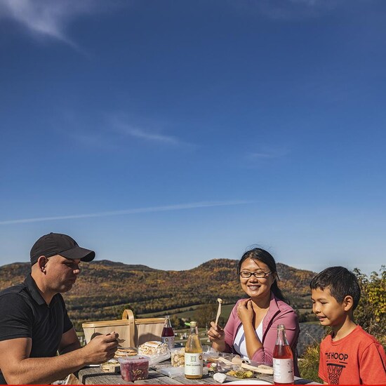 Trois personnes mangent à une table de pique-nique devant un panorama d'automne dans la région de Charlevoix.