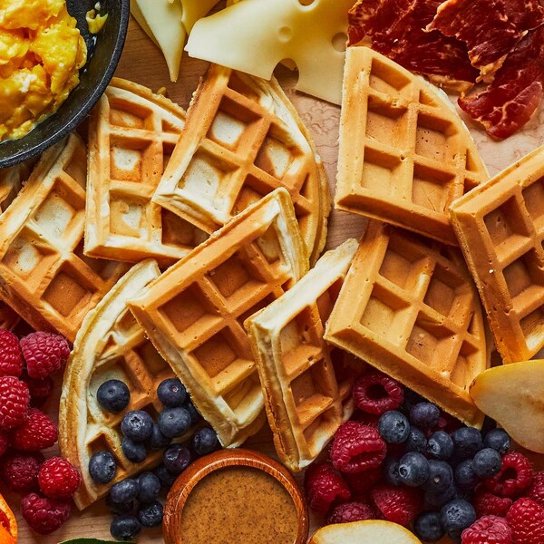 Des gaufres maison sur une planche de bois avec des garnitures salées et sucrées tout autour. 