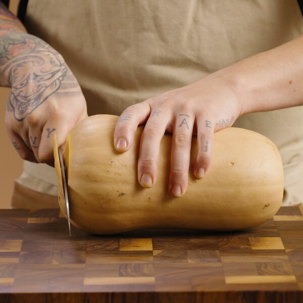 Une courge musquée est déposée sur une planche à couper, et deux mains la manipule pour la couper.