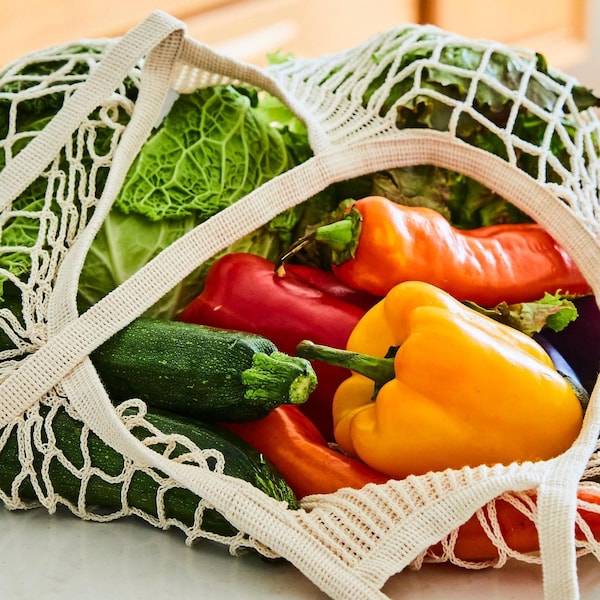 Des courgettes, des poivrons et un chou sont dans un sac tressé posé sur le dessus d'un îlot de cuisine. 
