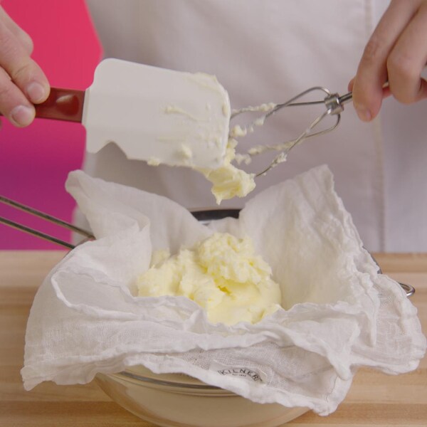 Une personne filtre son beurre en utilisant un torchon propre déposé sur un bol en verre. 